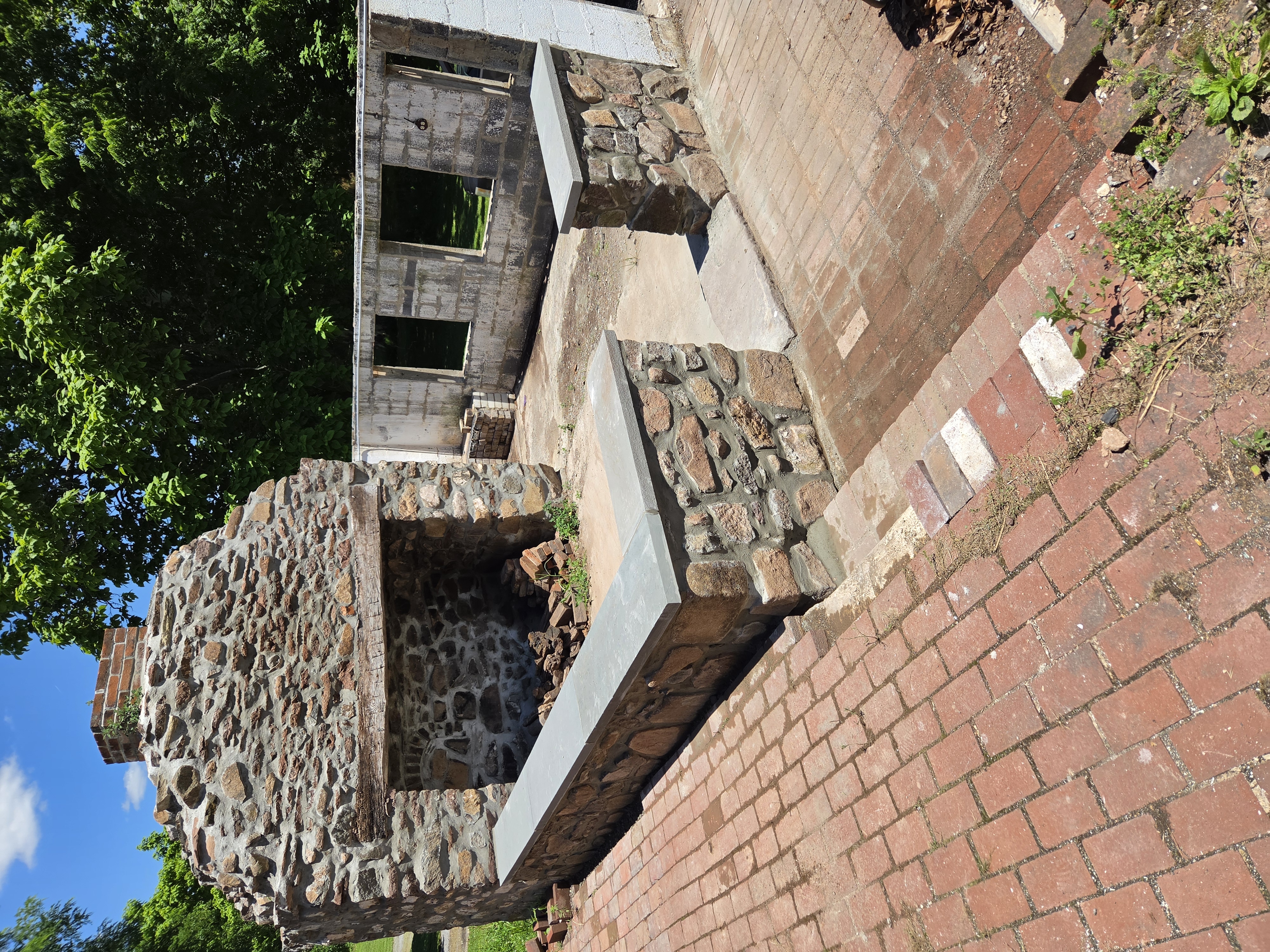 Completed freestanding stone sitting wall with capstone beside an 1800s outdoor kitchen in Birdsboro Pennsylvania